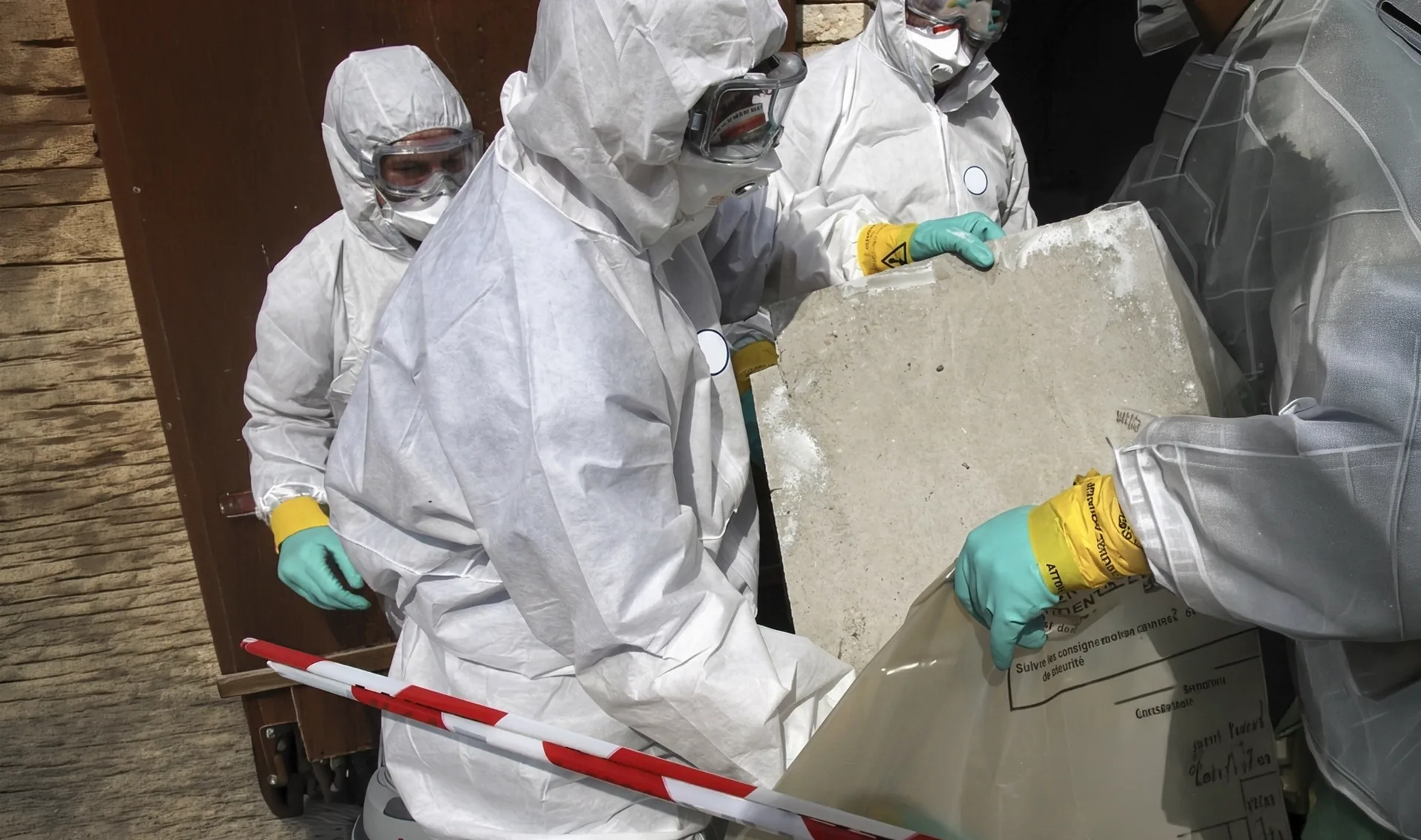 Opérateurs en combinaison étanche manipulant des plaques amiantées lors d'un chantier de désamiantage coordonné par Arkeom